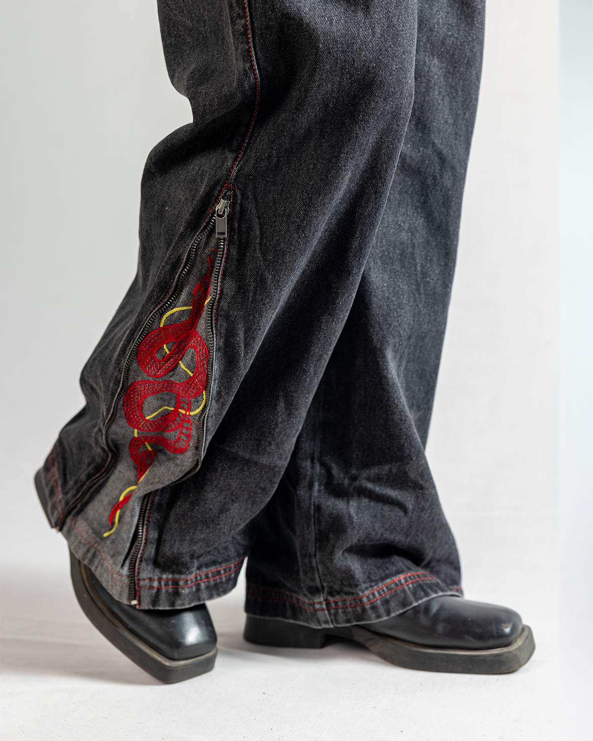 Black Year of Snake jeans featuring a unique zipper design and embroidered snake detailing.