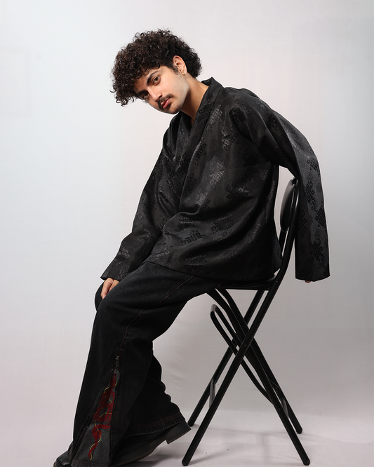 Wonju kimono shirt model wearing black shirt, seated on a chair, showcasing its relaxed elegant fit.